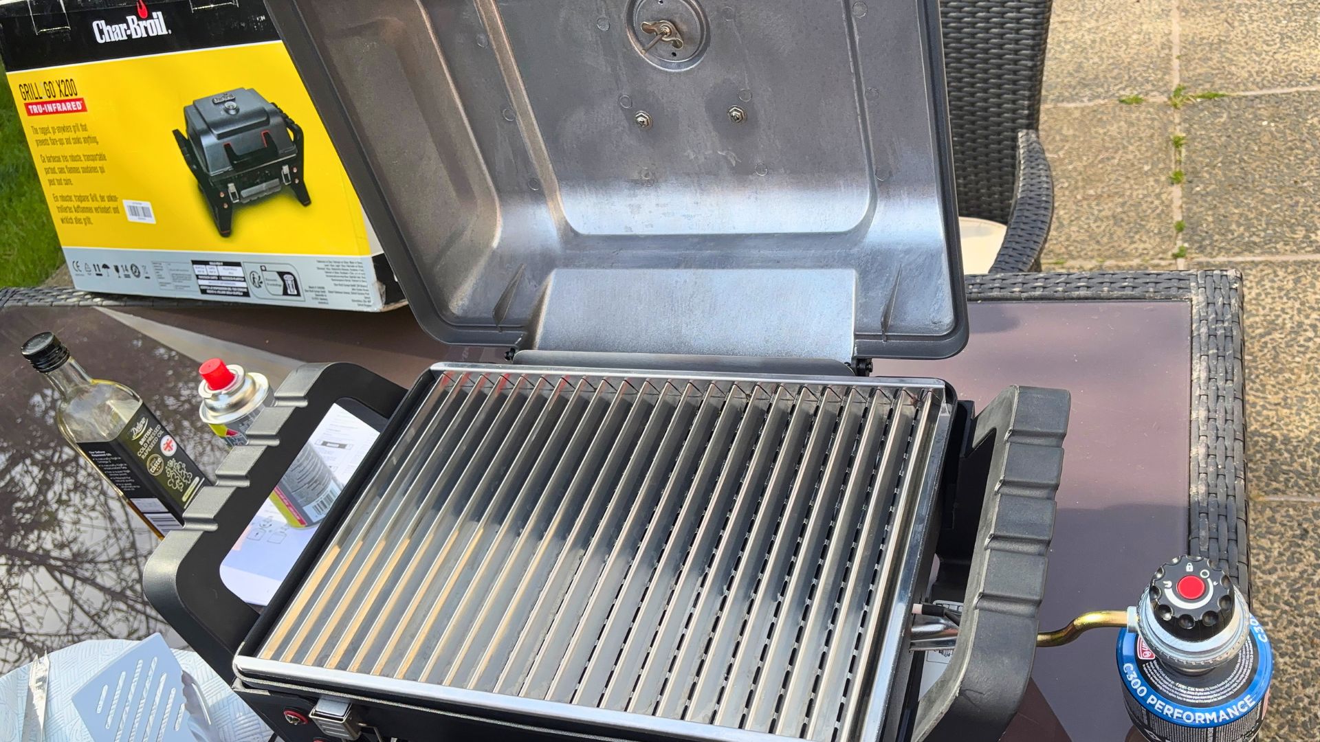The lid of a Char-Broil Grill2Go X200 open in a back garden, with the empty grill grates visible before being lit, ready for cooking during a sunny outdoor test.