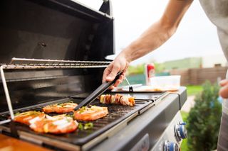 A man using tongs to flip meat on an outdoor grill