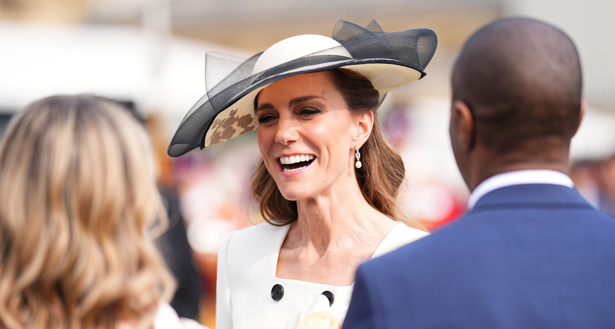 Princess Kate wearing a white hat smiling at guests at a garden party