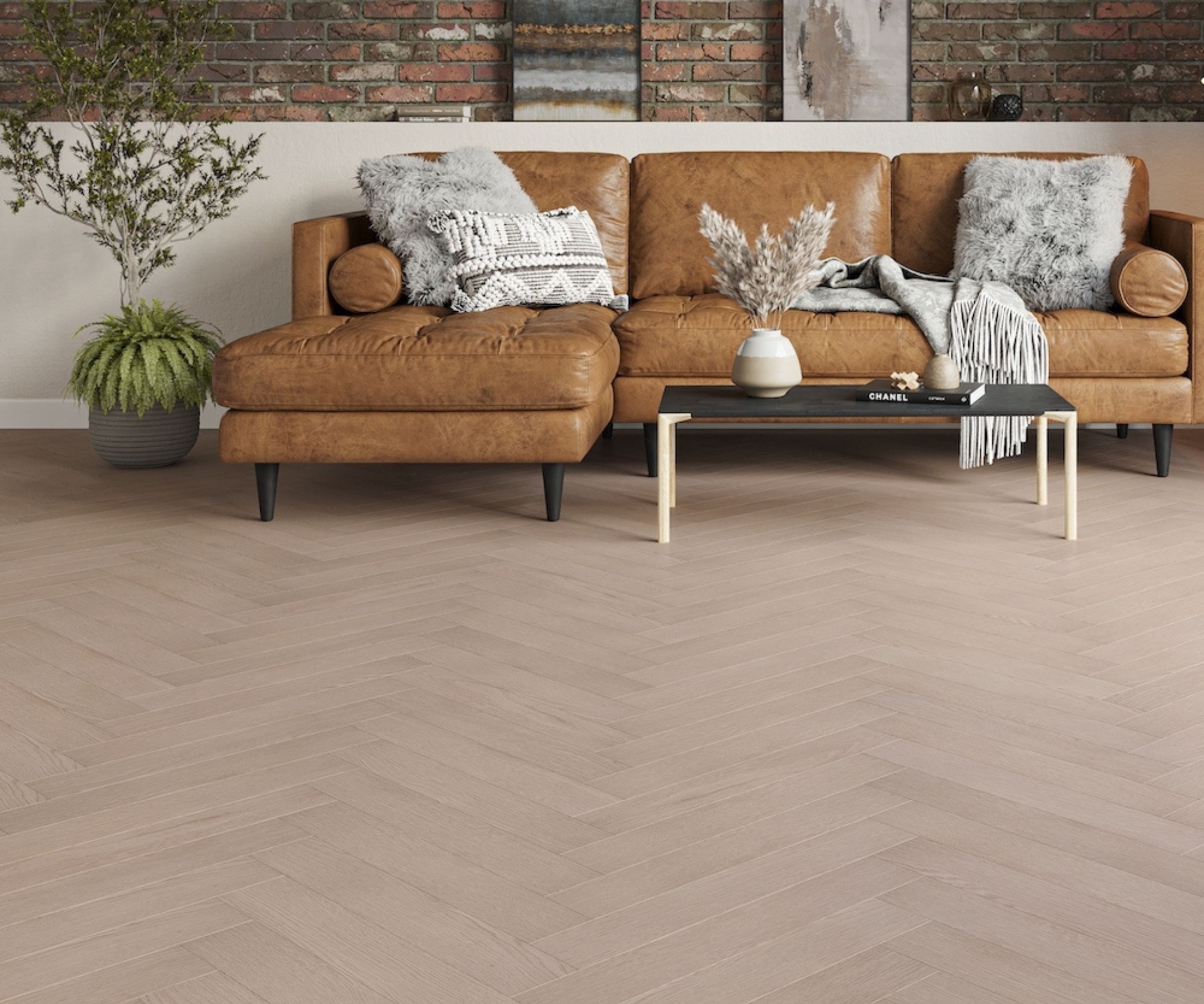A cosy living room with a tan leather corner sofa set against a brick wall. Pale herringbone wood flooring spreads across the room