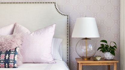 Learning how to update an outdated small bedroom is very useful. Here is a bedroom with lavender wallpaper, a white bed with lavender pillows, and a wooden nightstand