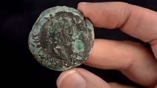 The profile of Roman Emperor Antoninus Pius on an ancient coin held in someone's hand. It is very worn.