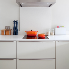 Two orange Le Creuset pans on a stove top in a modern white kitchen.