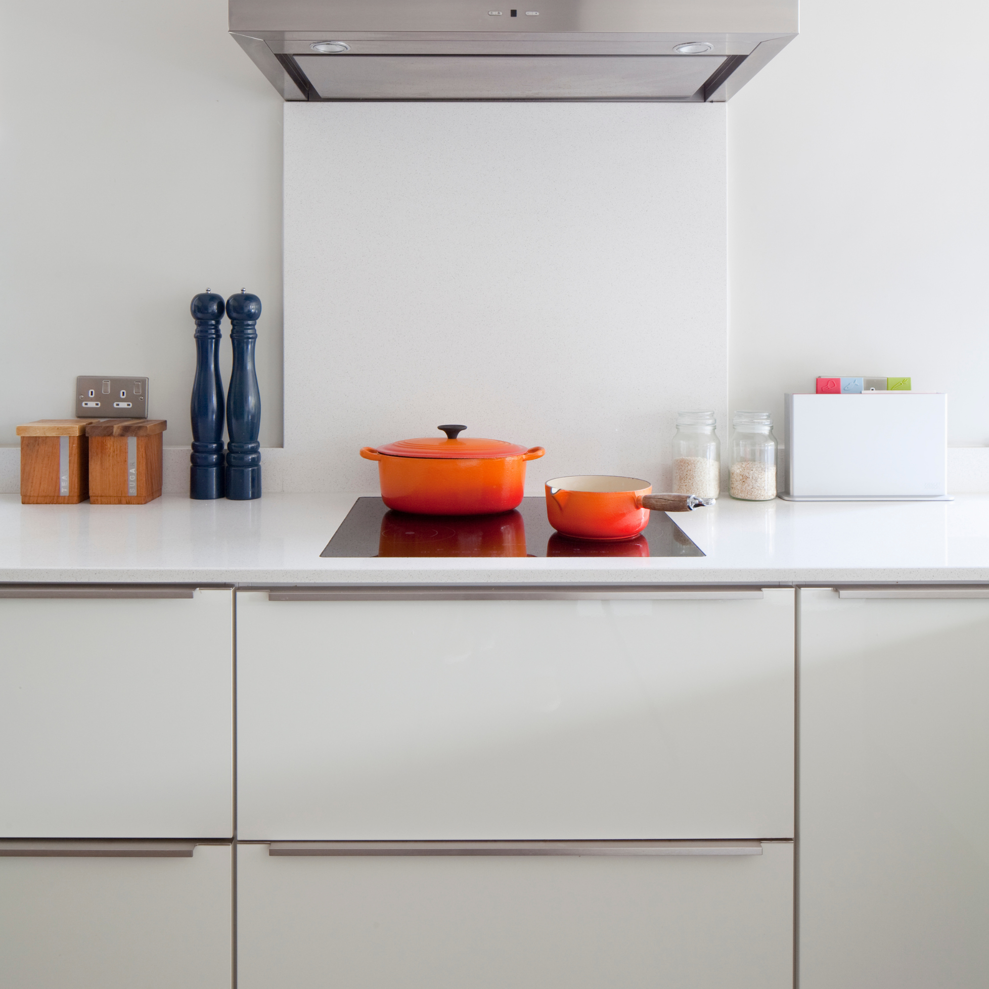 Two orange Le Creuset pans on a stove top in a modern white kitchen.