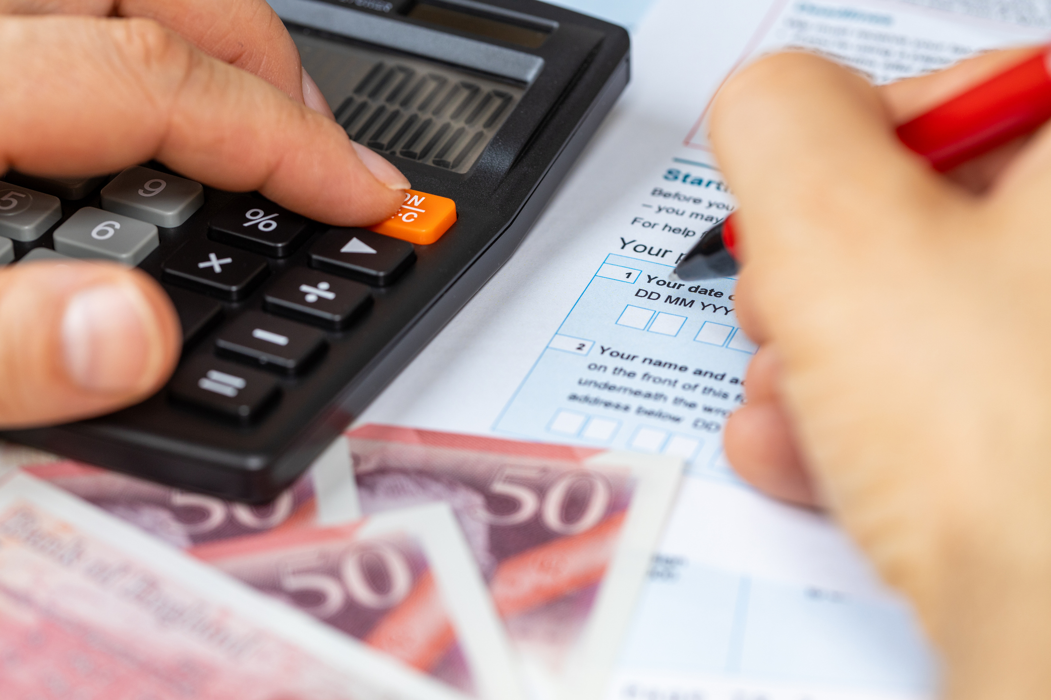 Person fills in tax form and uses calculator alongside some cash.