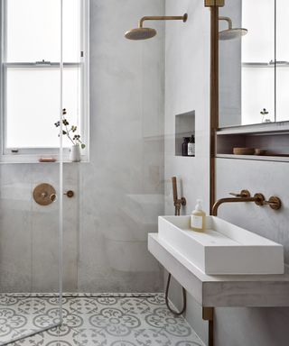 A wet room with gray and white mosaic floor tiles in the shower and a white sink attached to the wall