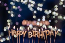 Candles spell happy birthday while glowing lights shine in the background. Festive moment of a birthday celebration at night.