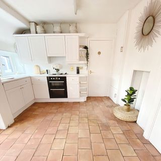 White kitchen with plant in woven pot on top of tiled floor with a framed mirror on the wall