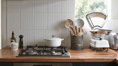 White kitchen worktop and oak shelving furnished with storage containers, trinkets and black KitchenAid stand mixer