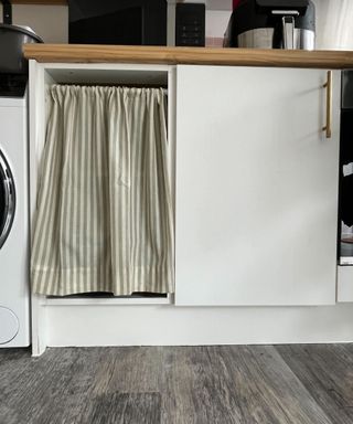 A tension rod being used to hang a green and white striped curtain in place of a cabinet door in a kitchen