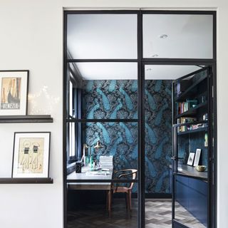 A small office with glass doors, painted dark blue with a feature wall, and parquet floor
