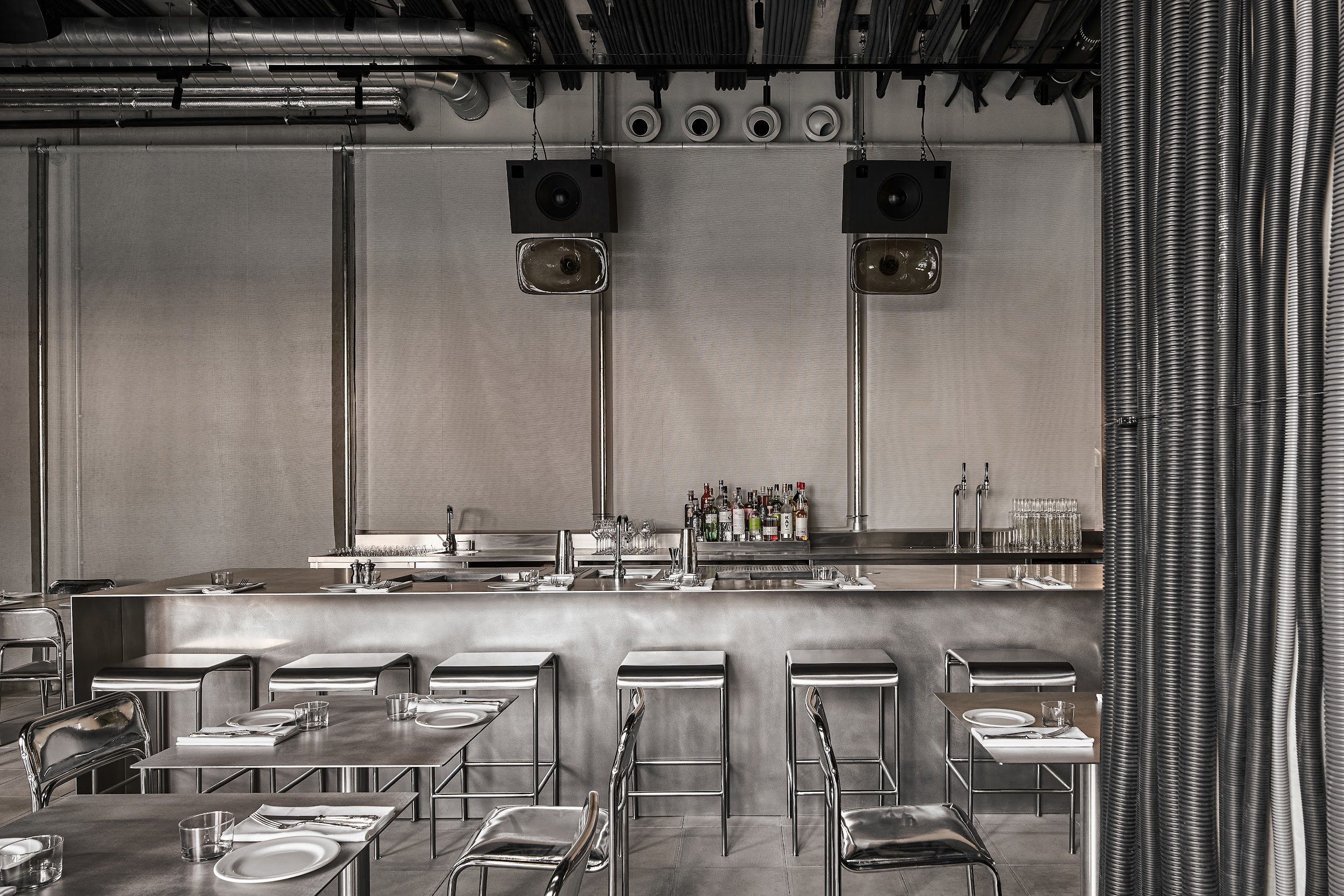 A chrome-clad restaurant features ceilings covered in exposed wires, metallic curtain, and matte silver surfaces.