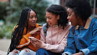 Young people in conversation, one of them holding a phone