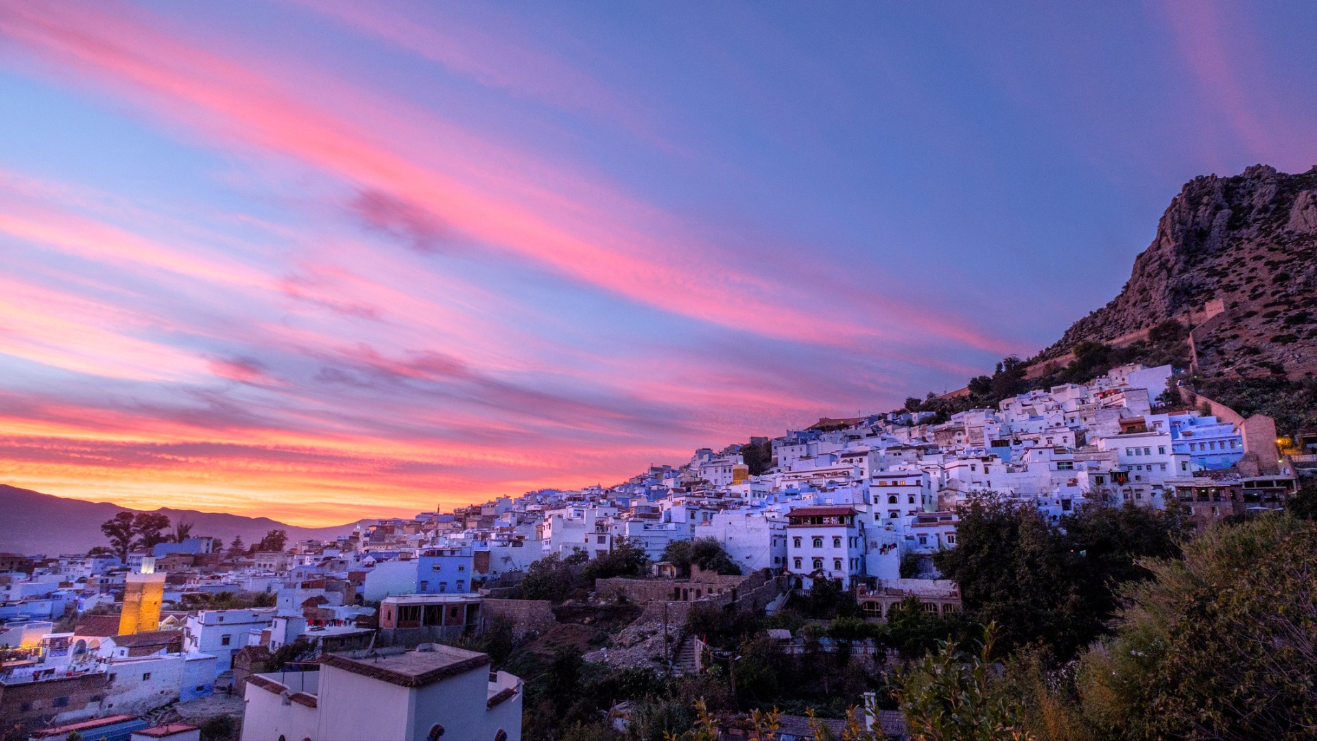 Blue-painted buildings nestled on a hillside under a vibrant pink and orange sunset.