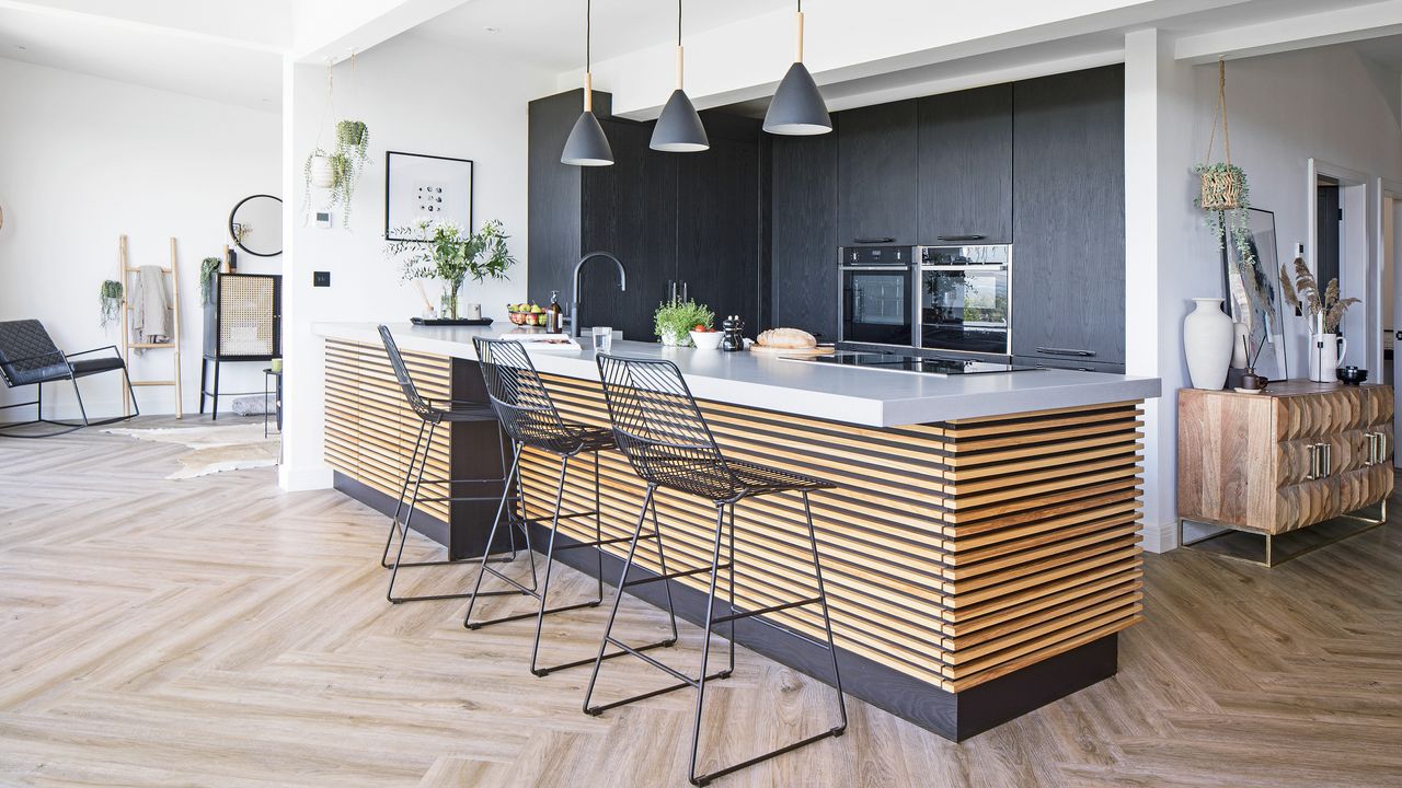 kitchen with wooden kitchen island, black wire chairs, wooden flooring, grey pendant lights 