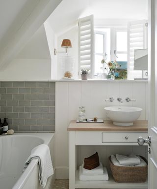 Cottage style bathroom with white walls, grey tile backsplash, white shutters, vanity with pine top