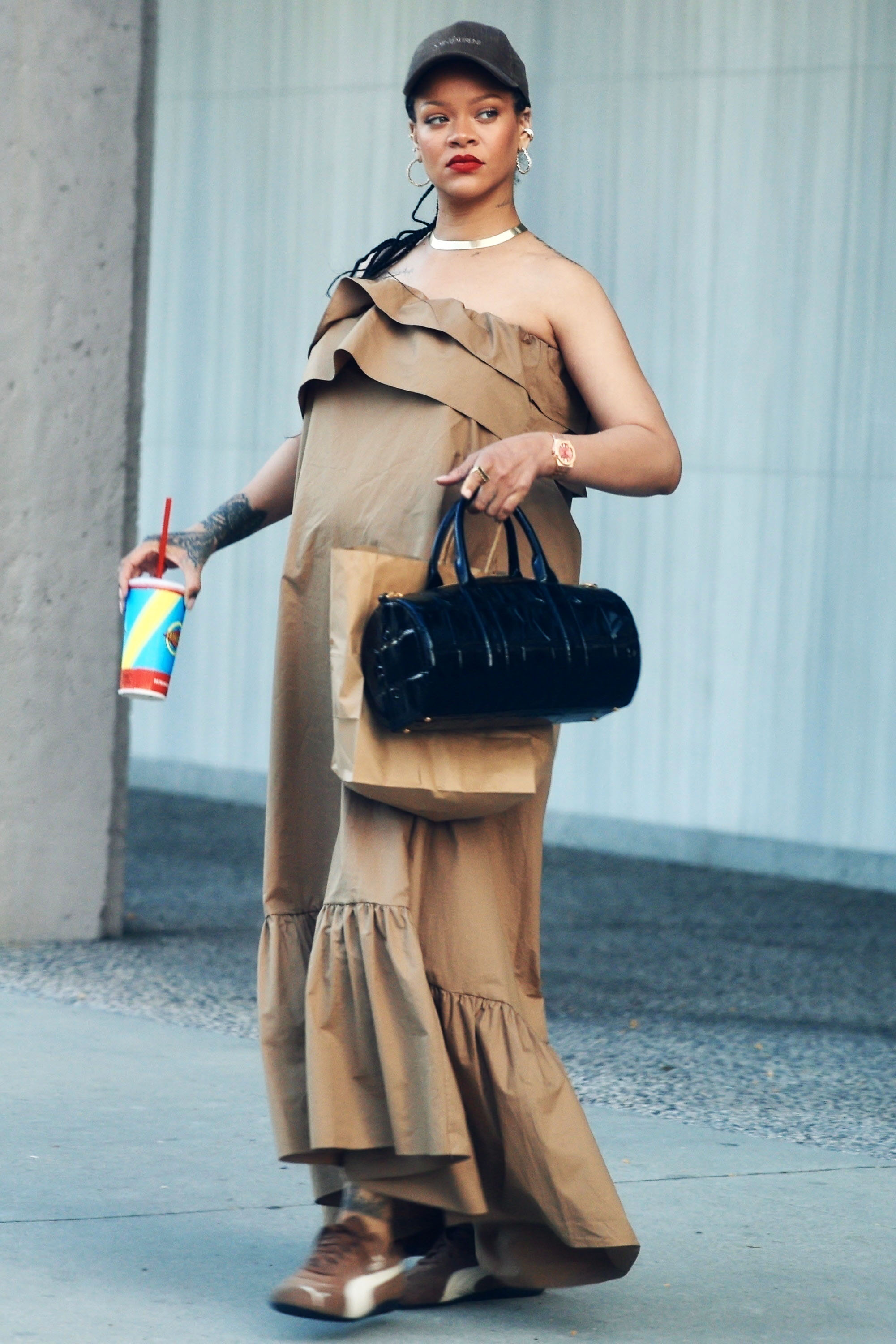 Rihanna wearing a brown strapless maxi dress, brown sneakers, a black baseball cap, and black bag in Los Angeles