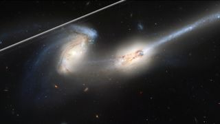 Hubble photo of two galaxies in deep space marred by a satellite trail, which appears as a bright white line across the upper left of the image.