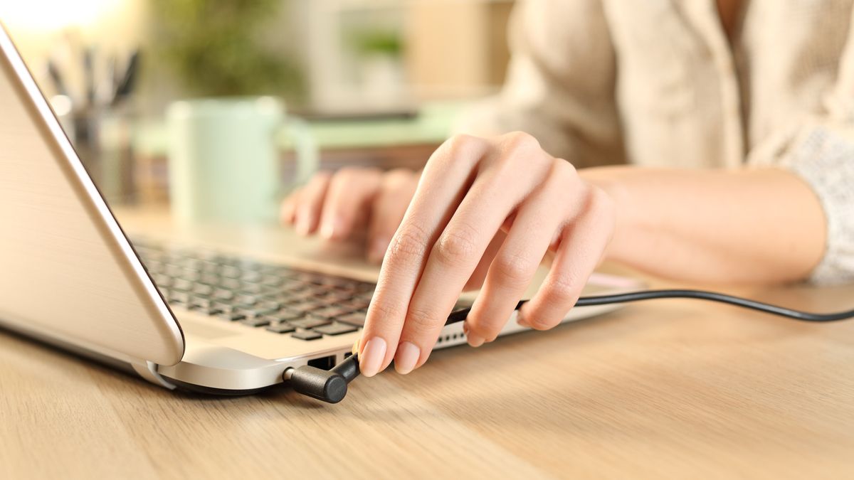 Close up of woman hands plugging battery charger on laptop at home