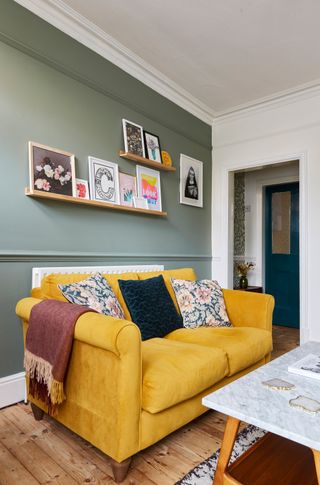 modern living room with a sage green wall, mustard sofa and picture rails with art prints