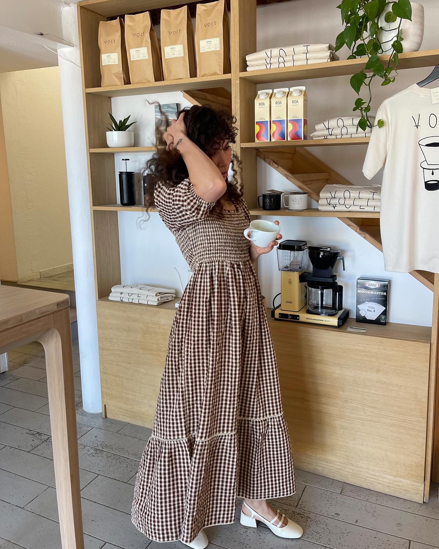 Woman in coffee shop wearing gingham dress and white shoes
