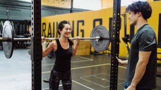 Fit female standing in a squat rack with a barbell on her shoulders in a gym, smiling