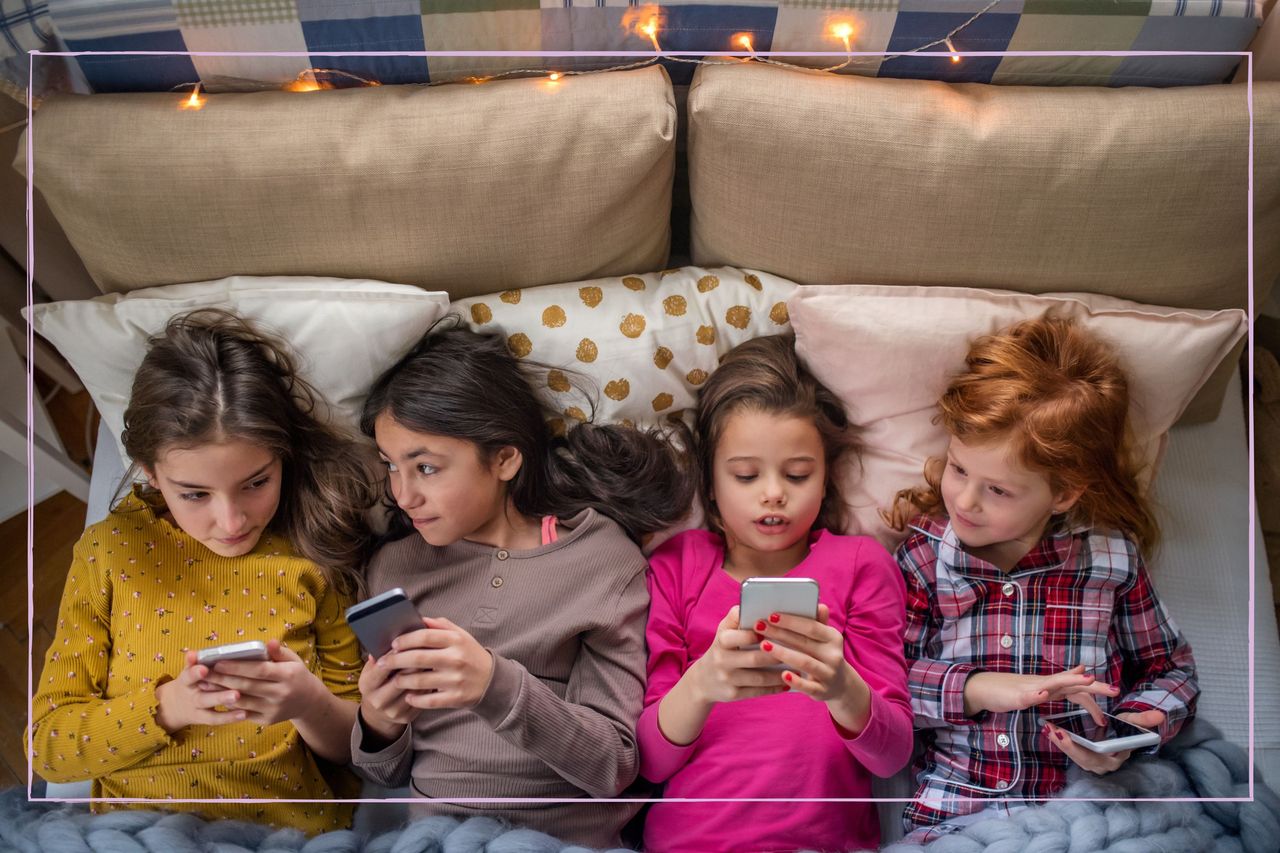 Four young girls lying in bed while looking at their smartphones