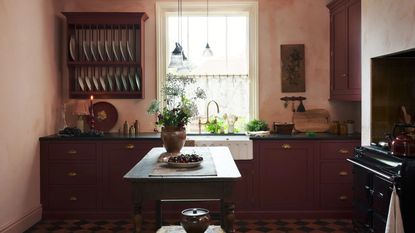 A vintage style kitchen painted in coral pink with ruby red cabinets and drawers. Above the countertop is also a plate rack. This small kitchen also has a small island in the middle of the space. 