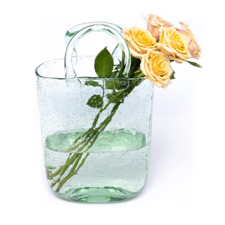 A clear glass vase shaped like a tall tote bag with yellow roses