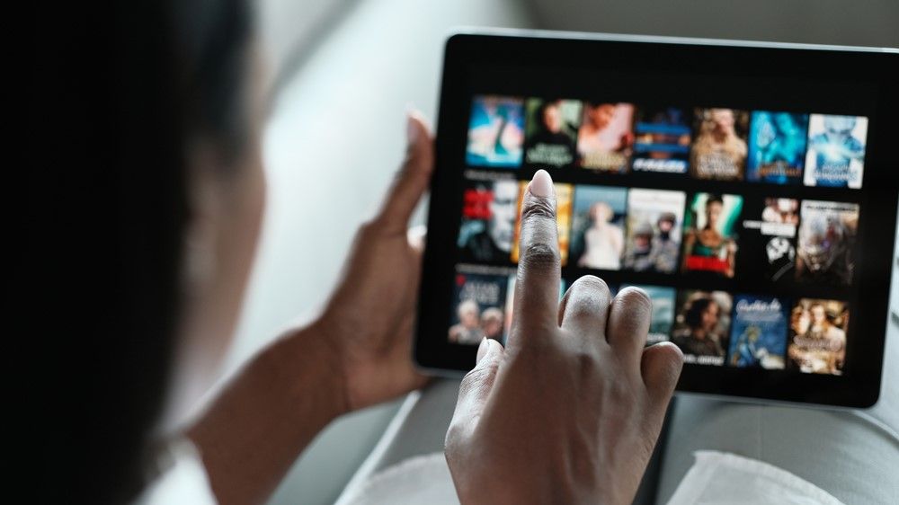 Woman holding tablet with streaming service on the screen, making a selection