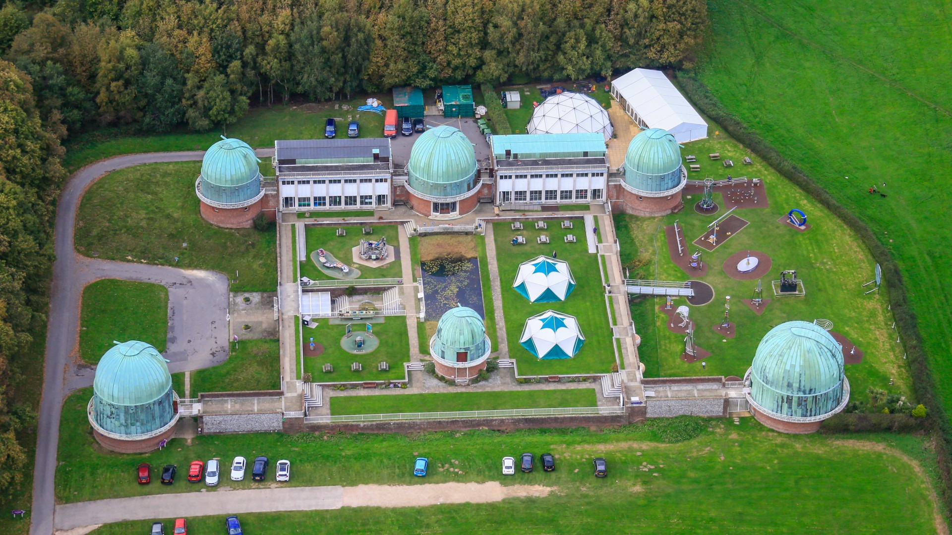 an aerial view of a complex of buildings that includes five domed structures surrounded by bright green pastures