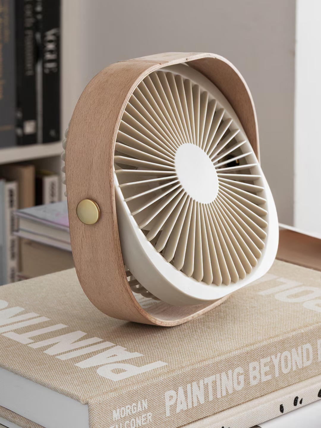 A minimalist beige fan from Printworks on a stack of coffee table books