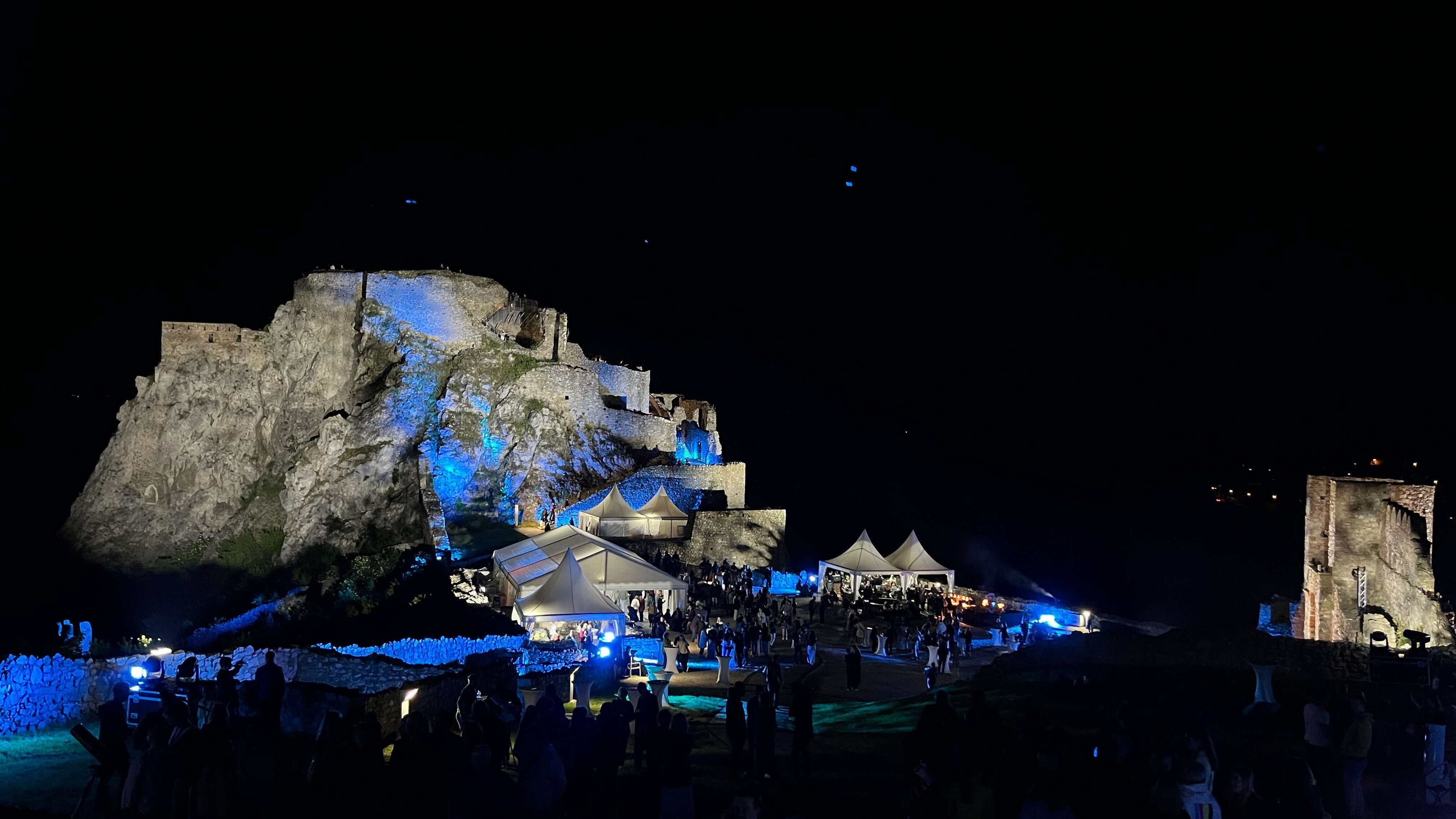castle ruins illuminated by blue lights with marquees below.