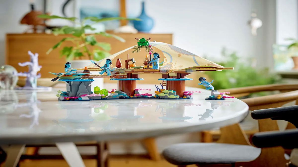Some blue minifigures are displayed among some stands connected with a canopy, all on a white table with plants and a wooden structure in the background.