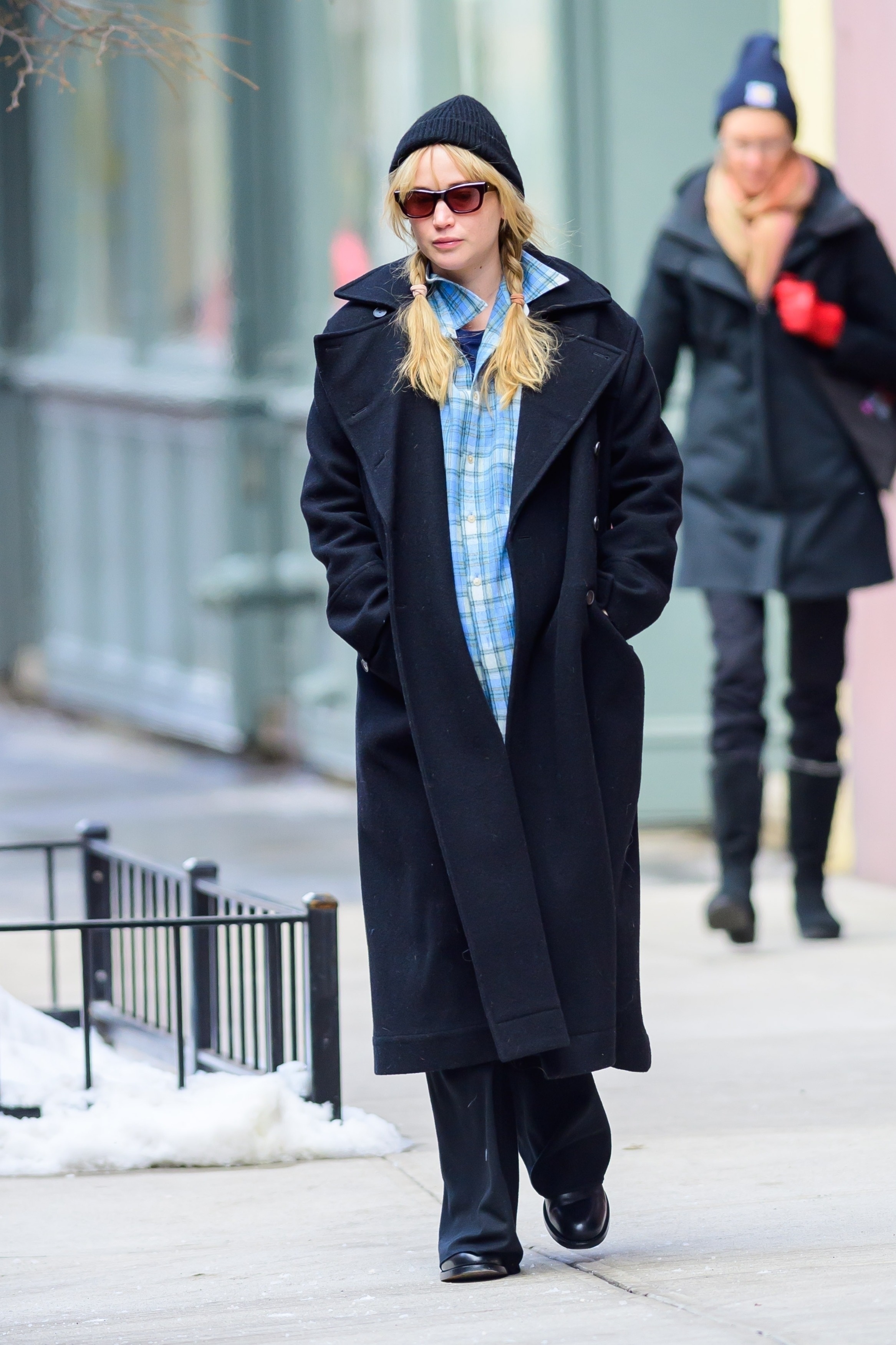 Jennifer Lawrence wearing a blue flannel shirt, a black wool coat, and black trousers