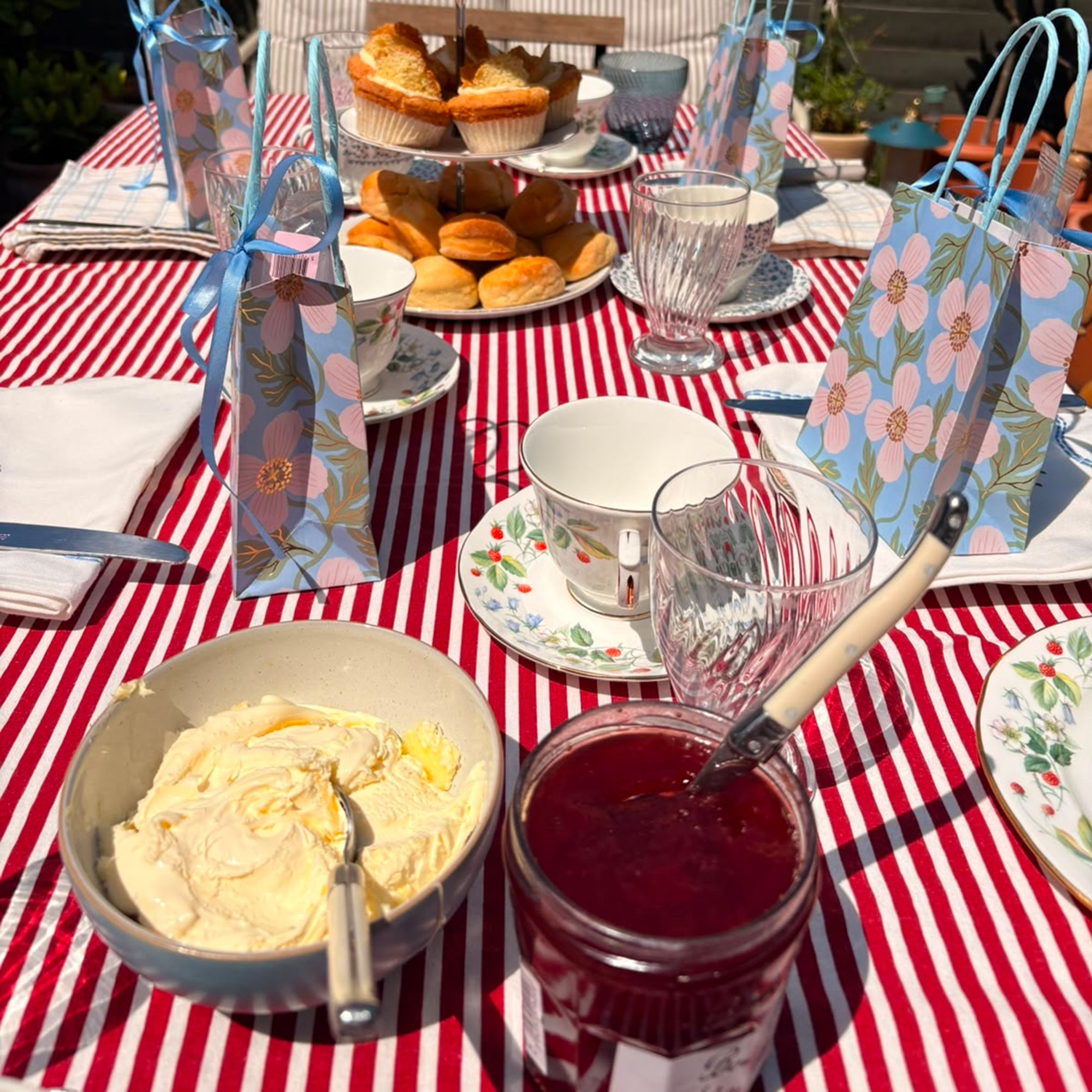 Red table cloth with bowl of clotted cream and jam, and tea cups
