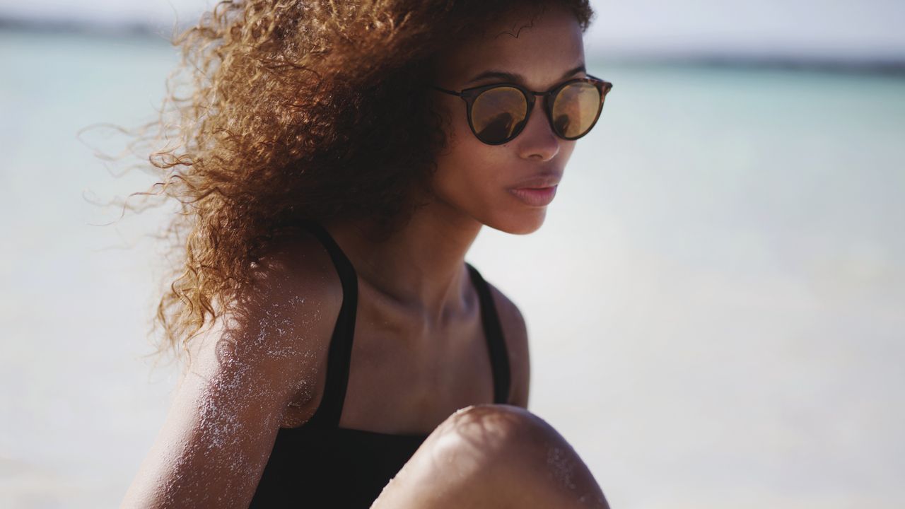 woman with curly hair sitting on beach