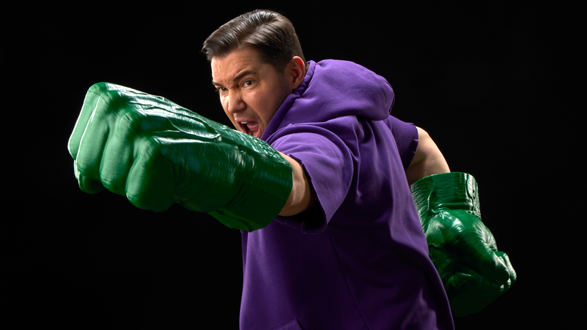 A man yells while punching with giant green Hulk Fists