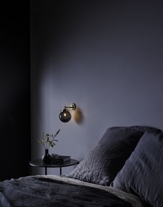 dark bedroom with wall light, black metal side table, dark bedding