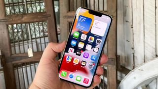 iphone 13 pro display on in hand with metal background, representing the hidden iPhone features everyone should know