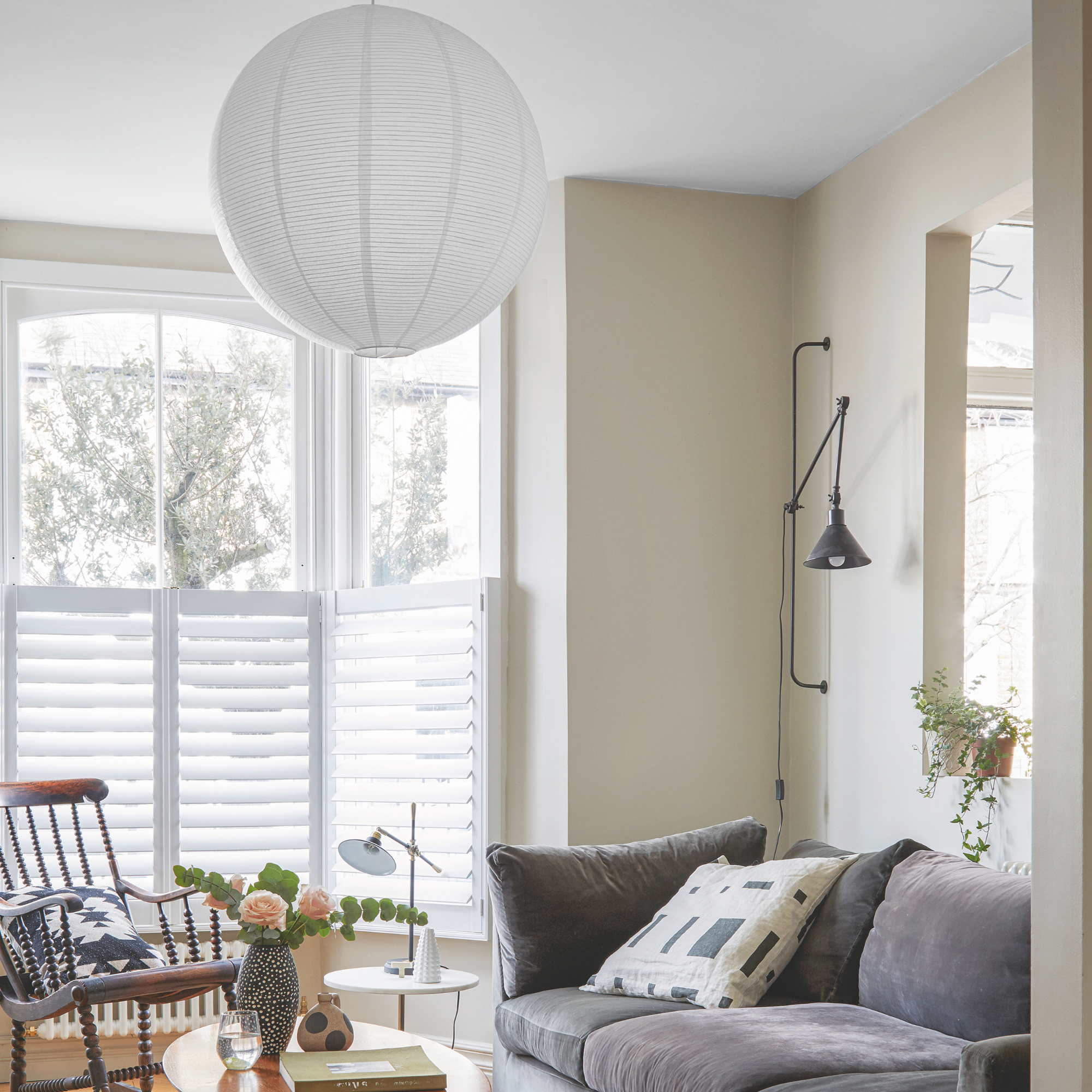 Living room with grey walls, wooden floor with grey rug and bay window with white blinds.