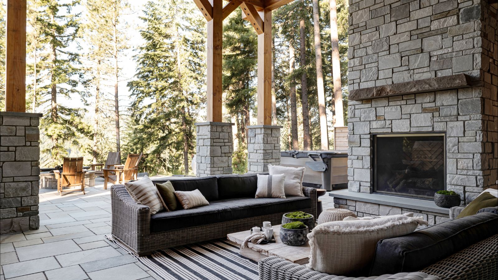 Outdoor patio with brick fireplace and sofas and fire looking out onto forest