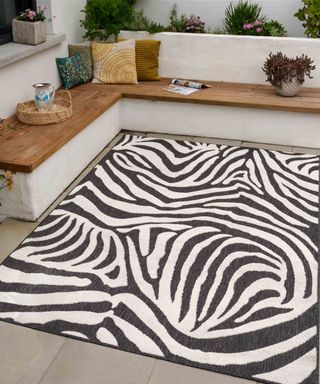 A monochrome zebra print outdoor rug in external backyard setting with seating area and potted plant decor