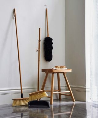 two brooms by wall with wooden stool and duster