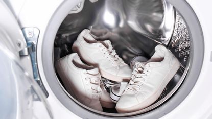 Two pairs of white shoes in a shiny white and metal washing machine 