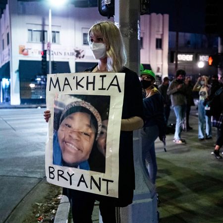 Lady on street corner wearing face mask holding post of Ma'Khia Bryant