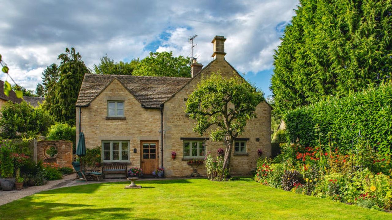 A cottage with a green lawn and tree border