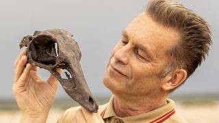Chris Packham in a beige top holds the fossilised skull of an ornithomimid dinosaur in Earth.