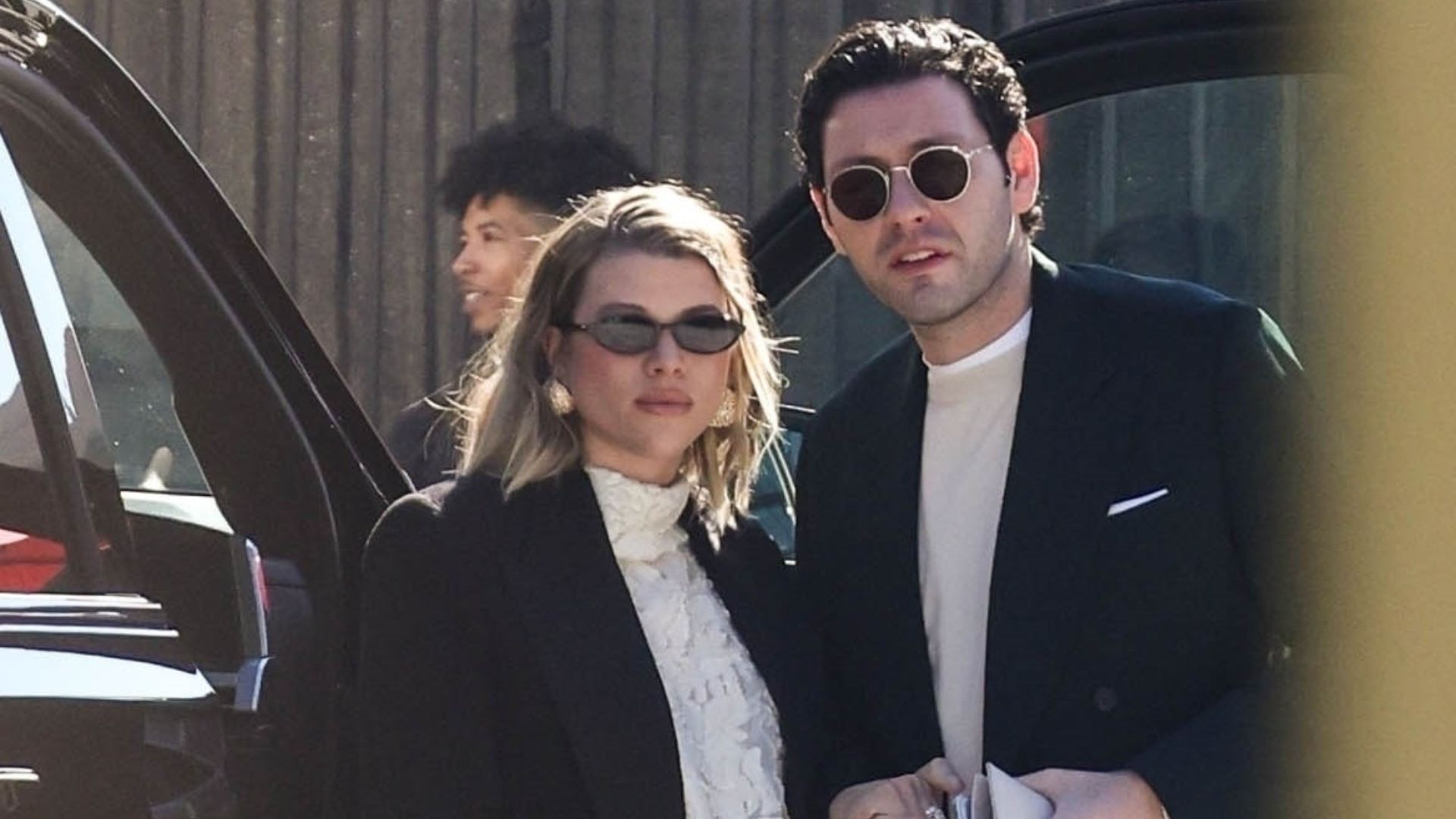 Sofia Richie wears a Schiaparelli two piece skirt set with a black coat, black bag and gold shoes.