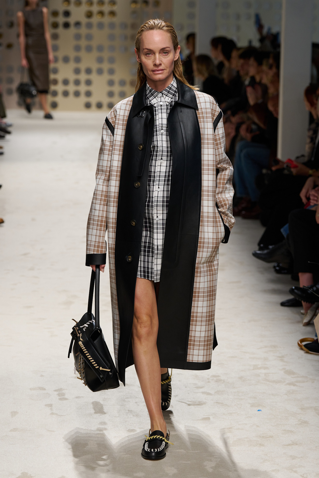 a model walking Tod's Spring 2026 runway wearing a black and white flannel shirt, flannel coat, and black loafers